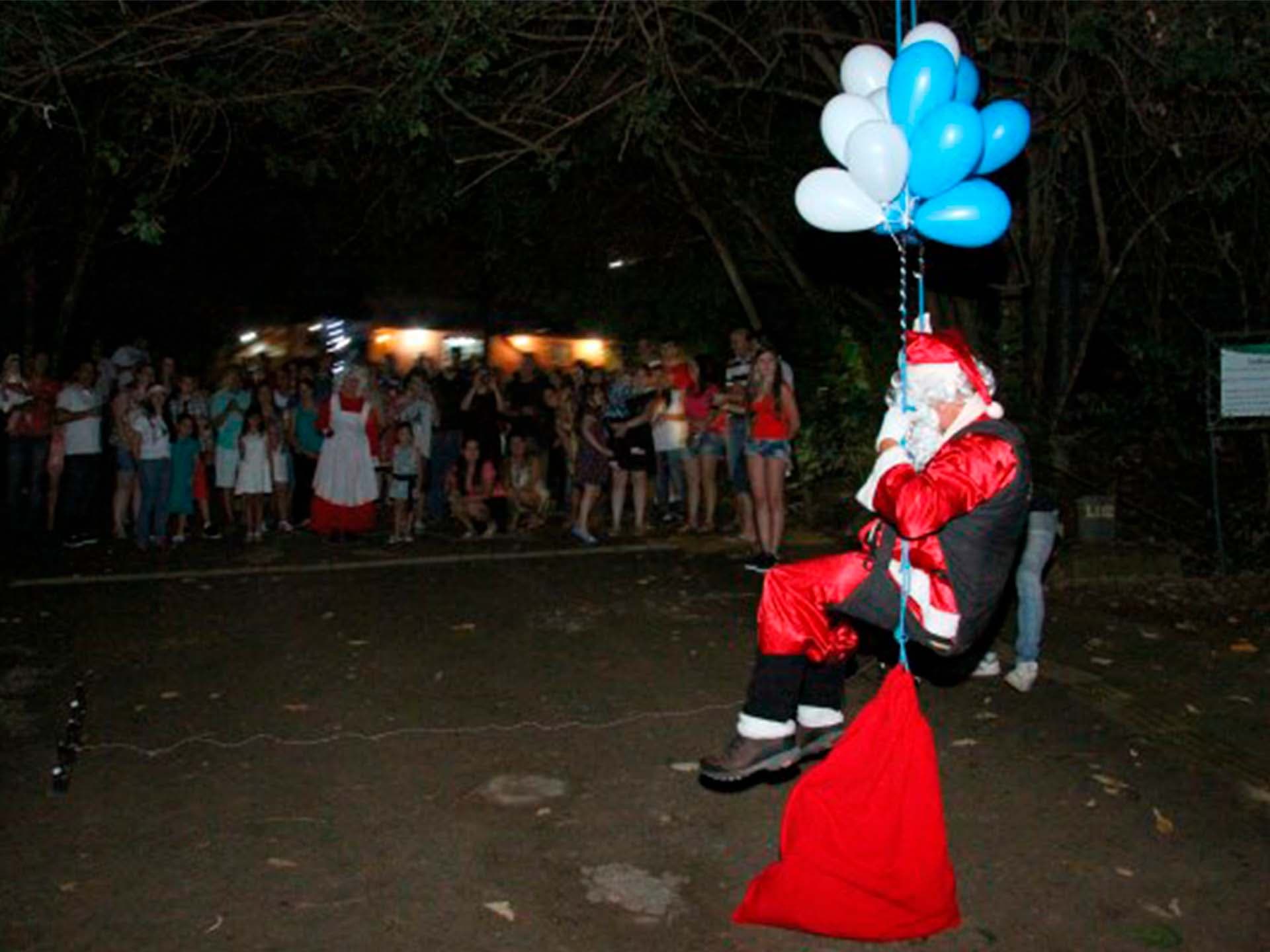 Papai Noel chegando preso a balões, recebido por famílias no hotel fazenda